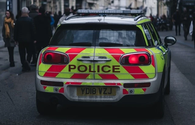 A British police car drives down a busy street with people walking on either
side of the car.
