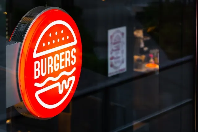 A red sign outside a restaurant that has the outline of a burger, with
Burgers written in place of the patty.
